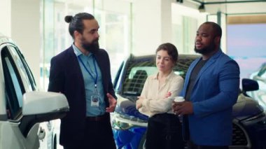 Araba satış temsilcisi müşterileri araç kapısına ve test kalitesine dokunmaya davet ederek bireylerin yatırım kararı almalarına yardımcı oluyor. Showroom temsilcisi müşterilerden otomobil özelliklerini, kamera A 'yı kontrol etmelerini istiyor.