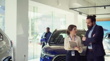 Satıcı kadın, tablet kullanarak adama seçenekler sunuyor. Satın alması için etki altına almaya çalışıyor. Showroom temsilcisi, aygıt, kamera B 'de ayrıntıları gösteren, istemciye uzatılmış garanti sunar