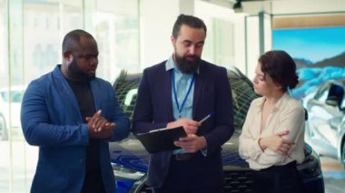 Satış temsilcisi müşterilere arabalar, finansman ve alım süreci hakkında sorular soruyor. Araç galerisi acentesi müşterilerin garantilerini, hizmetlerini ve mevcut ekstra özelliklerini açıklıyor, kamera A