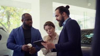 Araba galerisi satıcısının müşterilerine tablet üzerinde ürün sunumu yapması, uygun tavsiyelerde bulunması. Showroom temsilcisi, aygıt, kamera B 'deki müşterilere finansman seçenekleri sunar