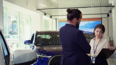 Satış elemanı müşteriyle konuşuyor, satın alma kararlarını neyin etkileyebileceğini anlamak için araç tipi, marka ve fiyat aralığını kavramaya çalışıyor, kamera B