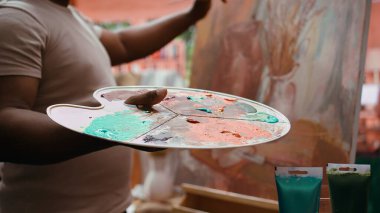 Kendine güvenen ressam palette farklı suluboyaları karıştırarak mükemmel gölgeyi yaratıyor ve güzel sanatlara, tuvale uyguluyor. Sanatçı canlı renkler ve dinamik fırça darbeleri kullanır. Kapatın. Kamera B.