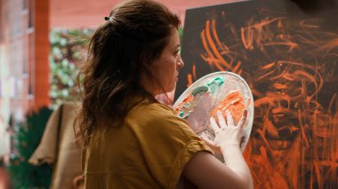 Ressam, son sanat eserinde parmak boyama tekniğiyle çalışır. Çağdaş sanat stüdyosu yaratıcılıkla uğuldar. Sanatçı canlı renkler ve modern boya tasarımı kullanır. Kamera A.