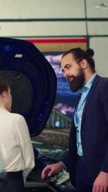 Müşterilere araç özellikleri hakkında derinlemesine bilgi sağlayan dikey video satış elemanı kaput altında kaliteli parçalar gösteriyor. Showroom temsilcisi müşterilerle motor gücü hakkında konuşuyor