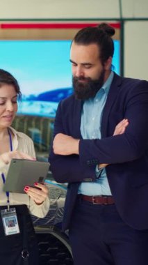 Dikey video satış elemanı erkek için araba kabul seçenekleri sunmak için tablet kullanıyor, satın alması için onu etkilemeye çalışıyor. Showroom temsilcisi, aygıtta ayrıntıları gösteren, A kamerasında geniş güvence sunar.