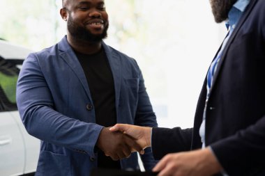 Pazarlık fiyatları ve ekstra araba özellikleri üzerine satış elemanı mutlu müşteriyle anlaşma yapıyor. Showroom temsilcisi onu satın almaya ikna ettikten sonra neşeli müşteriyle tokalaşıyor.