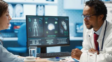 Tıbbi uzman oksimetre ile oksijen doygunluğu seviyelerini ölçüyor ve şarjörlü bir dijital cihazla yaşam belirtileri ölçümleri yapıyor. Doktor randevuda bir hastaya danışıyor. Kamera A.