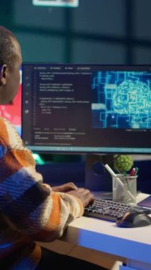 Dikey Video Profesyoneli erkek geliştirici, dizüstü bilgisayarda yapay zeka kodu ile çalışarak masasında nöral ağı yönetir. Afrikalı Amerikalı bilişim uzmanı serbest çalışan siber güvenlik geliştiriyor, güvenli veri tabanı yaratıyor.