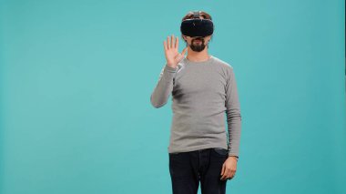 Sanal gerçeklik kulaklığı takan, arayüzle etkileşim kuran, hareketler yapan bir adam. İleri teknoloji modern VR cihazını kullanarak eğlenen kişi mavi stüdyo arka planında izole edilmiş, kamera A