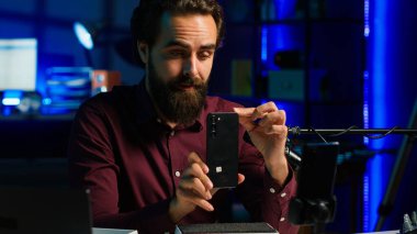 Neon lit stüdyosundaki medya yıldızı, markalı sponsorluk videosundan cep telefonunu sunuyor, özellikleri analiz ediyor. Nüfuz Edici, sosyal medya hesabı ve kamera A 'nın ardından teknoloji meraklılarının telefonlarını inceliyor.