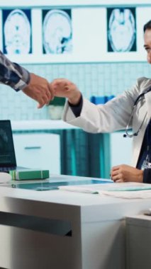 Dikey Video Hintli doktor ve hasta tıbbi danışmada el sıkışıyor sağlık kontrolünde sıhhiye geliyor. Modern klinikte sağlık hizmeti sağlayıcı hasta kişiye danışmanlık yapıyor. Kamera A.