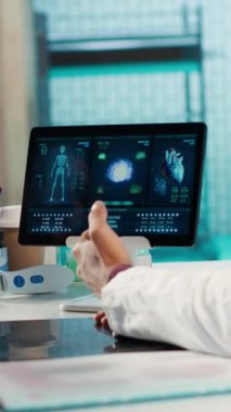 Kabinede tıbbi test sonuçlarını tartışmak için hastayla dikey video doktorları toplantısı, X-ray taramalarını yorumlamak için gelişmiş teşhis araçları kullanarak, profesyonel bir sağlık yaklaşımı göstererek,