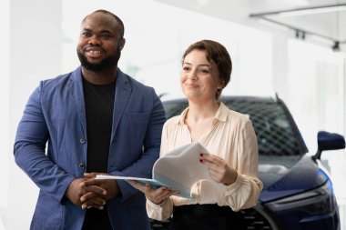 Araba galerisindeki mutlu müşteriler test sürüşüne çıkmadan önce otomobil kataloğuna bakıyor, özelliklerini ve özelliklerini kontrol ediyor. Neşeli müşteriler satın almadan önce araç modellerini karşılaştırıyor