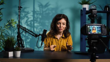 Mutlu çevrimiçi program sunucusu, bugünün video konusunu abonelerle konuşmak için mikrofon kullanarak profesyonel kamerada kayıt düğmesine basıyor. Yaratıcı video bloğunu kaydeden neşeli bir etkileyicidir