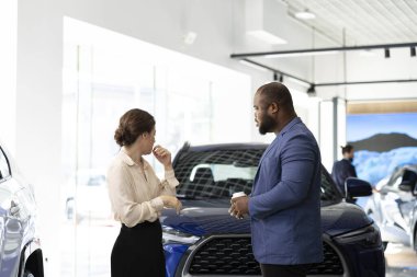 Araba galerisindeki müşteriler mevcut modellere bakıp ideal yatırım seçeneklerini seçmeye çalışıyorlar. Galeride araba almak isteyen karı koca, arabaları kontrol ediyor.