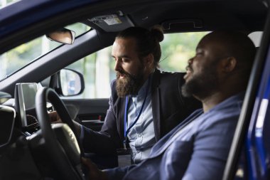 Araba satış yöneticisi test sürüşü sırasında müşteriye satış araçları gösteriyor, özelliklerini açıklıyor. Showroom satıcısı sürücünün aracı denemesine yardım ediyor, modelleri karşılaştırıyor