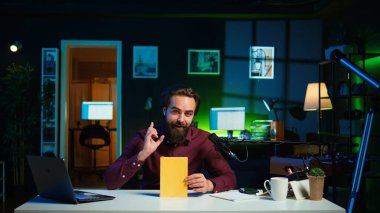 Stüdyodaki gülümseyen nüfuzlu yayınevinin yeni çıkan ciltli kitabını eleştiriyor. Yazardan okuyucuya yeni bir roman sunan mutlu akademisyen edebiyat videosu denemesi çekiyor