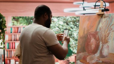 Yetenekli ressam, dijital pazarlama ve şöhret için çevrimiçi varlığını kullanarak, kendini tanıtmak için bitirdiği eserinin bir videosunu kaydediyor. Yeni sanat eseri içeriğiyle gurur duyuyor. Kamera A.