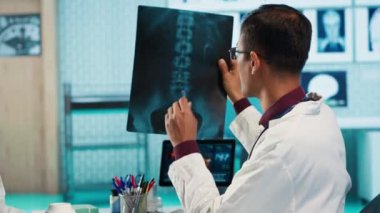 Hindistanlı sağlık uzmanı ofisteki bir hastayla tıbbi uzmanlığını paylaşıyor, doğru tedavi ve iyileşme için x-ray taramalarını ve MRI teşhislerini gözden geçiriyor. Sigorta danışmanlığı. Kamera A.