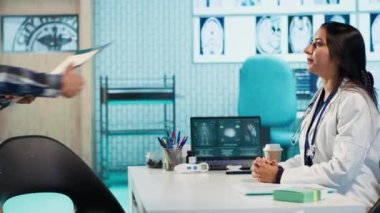 Bir kabinede tıbbi test sonuçlarını tartışmak için hastalarla yapılan doktor toplantısı, röntgen taramalarını yorumlamak için gelişmiş teşhis araçları kullanmak, profesyonel bir sağlık yaklaşımı sergilemek. Kamera A.