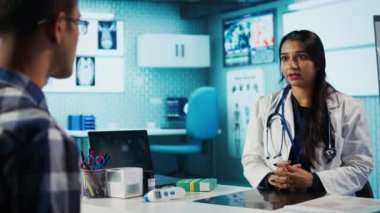 Tıbbi uzman ve hasta modern bir kabinede teşhis sonuçlarını tartışıyor, X ışını görüntüleme taramalarını sunmak için gelişmiş sağlık araçları kuruyor. Sigorta yönetimi. Kamera B.