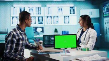 Hintli hekim, krom anahtarın yanındaki erkek hastaya danışmanlık yapıyor. Teknolojiyi tarama ve tanı koymak için kullanıyor. Sıhhiyeci kayıtlara dayanarak profesyonel tavsiye veriyor. Kamera A.