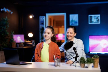 Neşeli çocuk ve annesi vlog kanalı girişini çekmek için profesyonel kayıt cihazlarını kullanarak içerik oluşturuyorlar. Kız ve ebeveyn hayran kitlesini selamlıyor.