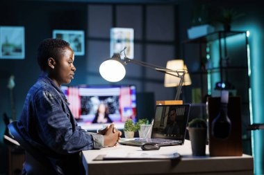 Siyah kadın dairesindeki dijital dizüstü bilgisayarında video konferansı yapıyor. Afro-Amerikalı kadın serbest çalışan masada oturuyor, evde çalışıyor ve kişisel bilgisayarda online toplantı yapıyor..