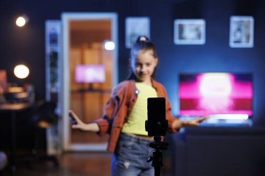 Çevrimiçi takipçileri için dans derslerini kaydetmek için kullanılan akıllı telefona odaklan. Bulanık arka plandaki Z jenerasyonundaki kız sosyal medyayı telefonla dolduruyor, coşkuyla dans hareketleri sergiliyor.