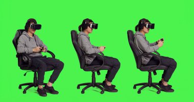 Genç adam, bir sürü aletle yeşil ekranın üzerinde telefon oyunları oynuyor, arkadaşlarıyla online oyun yarışmasına katılıyor. Asyalı erkek oyuncu VR kulaklığıyla neşeli hissediyor.