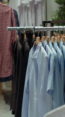 Dikey Video Zarif giyim mağazası rafları ve askıları çeşitli renklerde gömlekler seçerek, rafine edilmiş bir perakende alanında şık ve modaya uygun bir moda gösterisi yaratıyor. Boş alışveriş merkezi