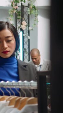 Dikey Video Tarzı kadın, modaya uygun kıyafetler ve canlı vitrinlerle çevrili modern bir butikte giyim seçeneklerini araştırıyor. Moda, tüketim ve perakende terapi gösteren Asyalı bir müşteri