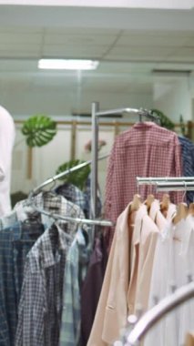 Dikey Video Tasarımcısı butik asistanı raflarda canlı bir kıyafet seçimi düzenliyor, şık yeni koleksiyon kıyafetlerini vurguluyor ve müşteriler için hoş bir alışveriş deneyimi yaratıyor