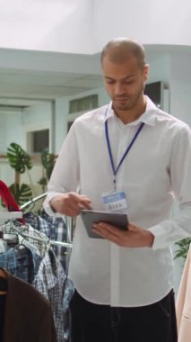 Dikey Video Alışveriş Merkezi çalışanı raflarda yeni moda koleksiyonu düzenliyor, kentsel perakende alanında moda kıyafetleri arayan müşteriler için bir görünüm kitabı konsepti sağlıyor. Modern alışveriş