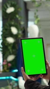 Dikey Videolu Asyalı perakende asistanı, giyim mağazasında yeşil ekranlı bir tablet tutuyor ve müşteriler için alışveriş deneyimini geliştiren şık bir vitrin yaratıyor. Çalışan bir alışveriş merkezinde çalışıyor..