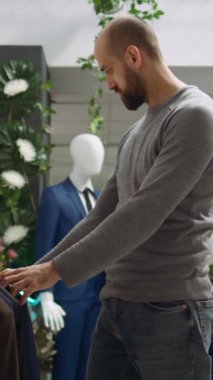 Dikey Video Modern Mağaza çalışanı müşteriye kıyafet seçeneklerini keşfetmede yardımcı oluyor, stil ve müşteri memnuniyetini sembolize ediyor. Moda uzmanlığını tartışan çeşitli adamlar. Kamera B.