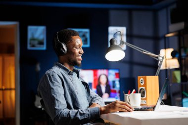 Çalışan evde podcast dinliyor ve yeni bir plan üzerinde çalışıyor. Sorumluluklarını yeni serbest sözleşme şartlarıyla çözüyor. Çevrimiçi yönetici bilgileri üzerine çalışan Afrikalı Amerikalı serbest çalışan.