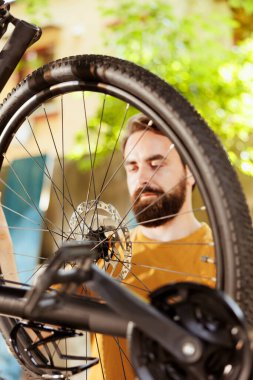 Detailed image showing different bicycle parts being inspected and repaired by active caucasian man outdoor. Sporty man checking bike tire for damages to fix with work tools in yard clipart