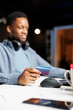 Afrikalı Amerikalı bir adam internet sitesinden kart numaralarını giriyor ve online mağazadan kıyafet siparişi almaya hazırlanıyor. Genç yetişkin, dizüstü bilgisayarda alışveriş sırasında elektronik bankacılık işlemi kullanıyor.
