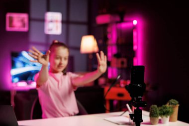 Tripoddaki telefon, çocuklara okulda alınan yüksek notları anlatmak için heyecanlı bir çocuk tarafından kullanıldı. Bulanık arka planda sevimli bir kız akıllı telefonuyla aile kanalını çevrimiçi yayınlamak için video çekiyor