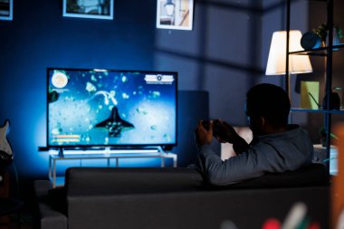 Evde, konsol oyuncusu gece arkadaşlarıyla dünya çapında silah ateşleme yarışması düzenlemek için oyun oynamak için yarışıyor. Genç oyuncu 4k televizyon ekranında video oyunu şampiyonluğunun keyfini çıkarıyor.