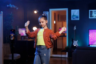 Sosyal medya ağlarında büyüleyici dans figürleri sergileyen sevimli bir kız, viral bir meydan okumaya katılıyor. Neşeli Z dansçısı internet izleyicileri için stüdyo dairede video kaydı yapıyor