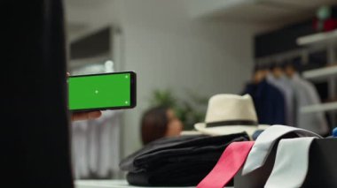 Erkek mağaza çalışanı telefonda fotokopi çekiyor ve moda gösterisi ve tüketim için koridorda renkli aksesuarlar düzenliyor. Orta Doğulu adam kemer ve kravat koleksiyonunu sınıflandırıyor.