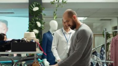 Alışveriş merkezindeki giyim mağazası çalışanı alışverişçiye moda tavsiyesi veriyor, kişisel stil rehberliğini vurguluyor ve modern bir butikte perakende alışveriş deneyimini geliştiriyor. Kamera A.