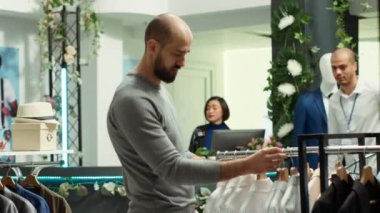 Modern stil mağazası çalışanı müşteriye kıyafet seçeneklerini keşfetmede yardım ediyor, stil ve müşteri memnuniyetini sembolize ediyor. Moda uzmanlığını tartışan çeşitli adamlar. Kamera A.