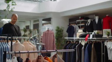 Asyalı kadın mağaza çalışanı askılarda yeni tasarımcı kıyafetleri düzenliyor, şık ve yeni moda kıyafet koleksiyonunu geliştiren bir moda gösterisi düzenliyor. Kamera B.