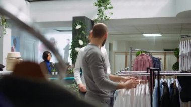 Moda mağazası çalışanı erkek müşteriye tarz seçimlerinde yardımcı oluyor, müşteri hizmetlerini vurguluyor ve kaliteli giysilerin yeni koleksiyonunu sunuyor. Kişisel alışveriş deneyimi. Kamera B.