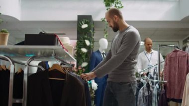 Modern stil mağazası çalışanı müşteriye kıyafet seçeneklerini keşfetmede yardım ediyor, stil ve müşteri memnuniyetini sembolize ediyor. Moda uzmanlığını tartışan çeşitli adamlar. Kamera B.