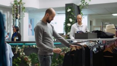 Alışveriş merkezi çalışanı, müşteriye yeni kıyafet koleksiyonundan seçmesi için yardım ediyor, kumaşın kalitesini ve potansiyel çeşitlerini sunuyor. Güzel alışveriş deneyimi. Kamera B.