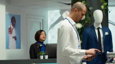 Perakende satış asistanı modaya uygun bir butikte raflardaki kıyafetleri inceliyor, müşteriler için ürün seçenekleri hazırlıyor. Orta Doğulu adam moda tutkusu, kaliteli tasarımcı kıyafetleri. Kamera A.